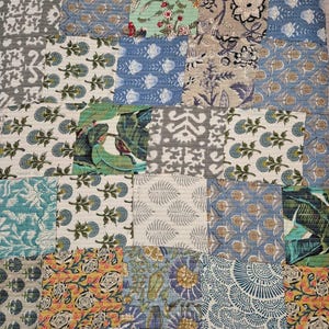 May include: A patchwork quilt featuring a variety of floral and geometric patterns in shades of blue, green, gray, and yellow. The quilt is made of multiple fabric squares sewn together, creating a textured and colorful design.