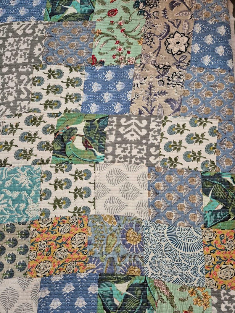 May include: A patchwork quilt featuring a variety of floral and geometric patterns in shades of blue, green, gray, and yellow. The quilt is made of multiple fabric squares sewn together, creating a textured and colorful design.