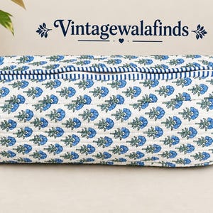 May include: A rectangular quilted fabric pouch featuring a repeating blue and green floral block print pattern on a white background. The pouch has a blue and white striped zipper closure and a matching striped fabric pull tab on the side.