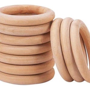 May include: A stack of eight unfinished wooden rings and a separate group of three. The rings are light brown and appear to be made of natural wood. The rings are smooth and round, with a hole in the center.