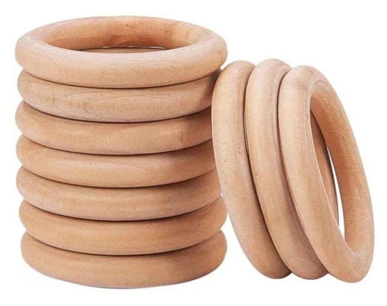 May include: A stack of eight unfinished wooden rings and a separate group of three. The rings are light brown and appear to be made of natural wood. The rings are smooth and round, with a hole in the center.