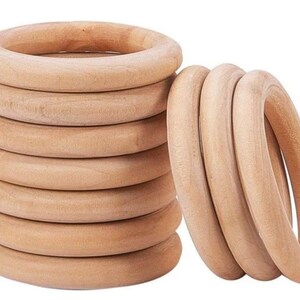 May include: A collection of unfinished wooden rings, perfect for crafting or educational toys. The rings are a light, natural wood color, with a smooth, rounded shape. Some rings are stacked, while others are grouped together.