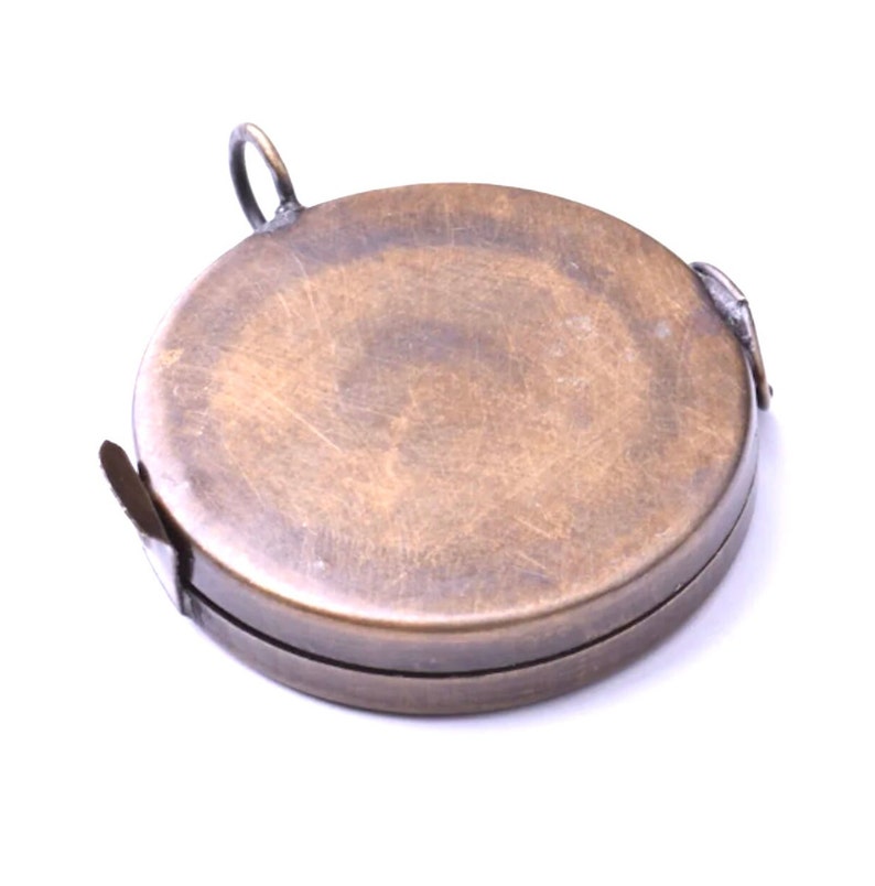 May include: A round, brass measuring tape with a hinged lid and a small loop on top. The tape is closed and appears to be vintage.