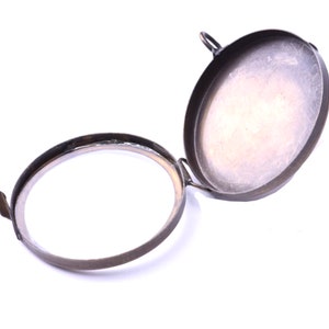 May include: A round, brass, hinged locket with a smooth, slightly worn surface. The locket is open, revealing the empty interior.
