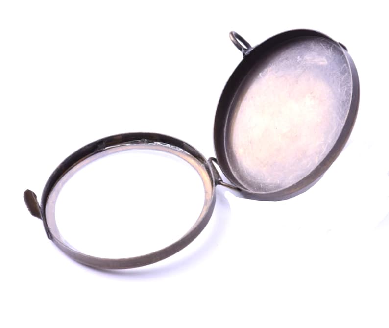 May include: A round, brass, hinged locket with a smooth, slightly worn surface. The locket is open, revealing the empty interior.