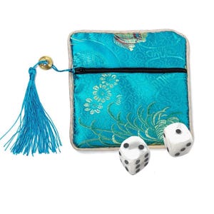 May include: A square turquoise fabric pouch with a black zipper closure, featuring a floral pattern and a long matching turquoise tassel attached by a gold-toned coin charm. Two white six-sided dice with black pips are positioned in front.