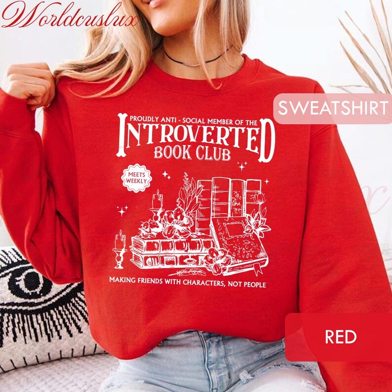 May include: A red sweatshirt with white text and graphics. The text reads "INTROVERTED BOOK CLUB" with the phrase "MAKING FRIENDS WITH CHARACTERS, NOT PEOPLE" below an illustration of books, candles, and flowers. The word "SWEATSHIRT" is in the upper right corner.