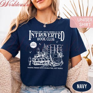 May include: Navy blue unisex shirt with a white graphic that reads "Introverted Book Club." The design includes illustrations of books, candles, and floral elements. The text "Making friends with characters, not people" is also included.
