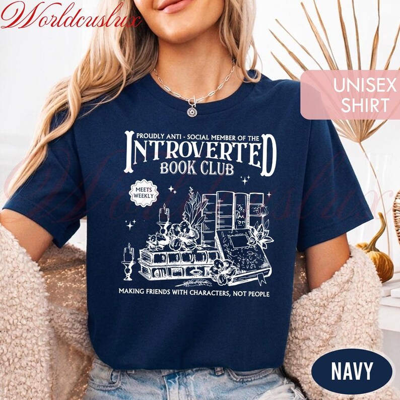 May include: Navy blue unisex shirt with a white graphic that reads "Introverted Book Club." The design includes illustrations of books, candles, and floral elements. The text "Making friends with characters, not people" is also included.