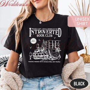 May include: Black unisex t-shirt with a white graphic design featuring the text "INTROVERTED BOOK CLUB" and illustrations of books, candles, and plants. The shirt also includes the phrase "MAKING FRIENDS WITH CHARACTERS, NOT PEOPLE."