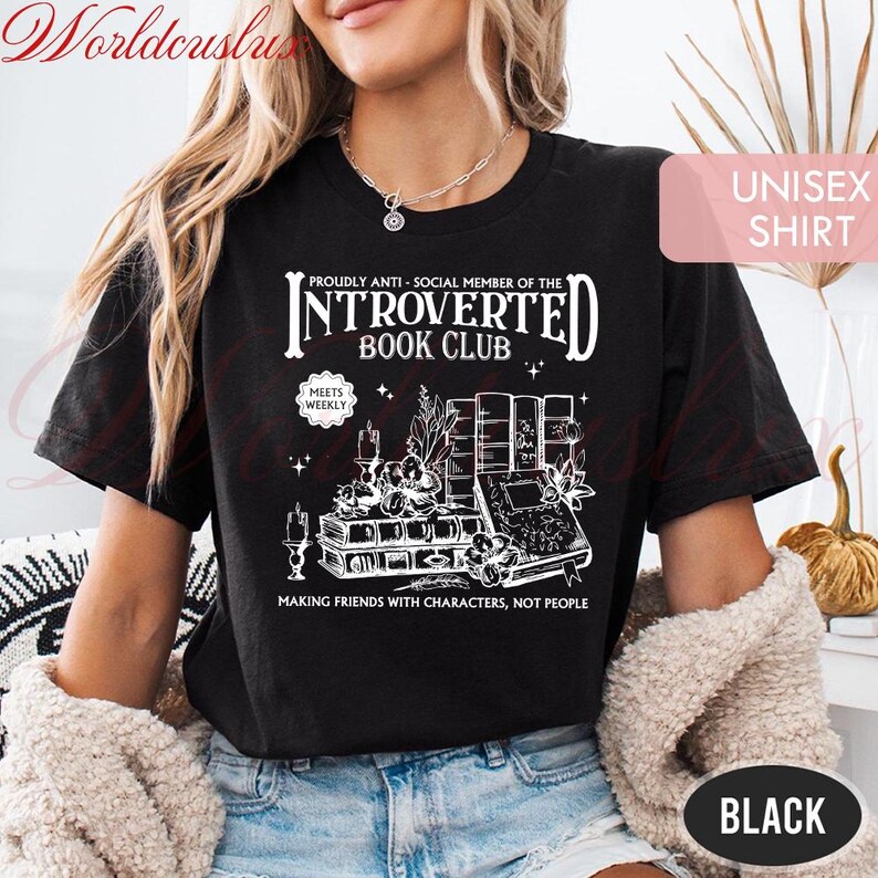 May include: Black unisex t-shirt with a white graphic design featuring the text "INTROVERTED BOOK CLUB" and illustrations of books, candles, and plants. The shirt also includes the phrase "MAKING FRIENDS WITH CHARACTERS, NOT PEOPLE."