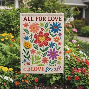 May include: A garden flag with the words "ALL FOR LOVE" and "and LOVE for all" in burgundy and blue. The flag features colorful flowers in red, yellow, blue, and purple with green leaves. The flag is displayed on a black metal stand.