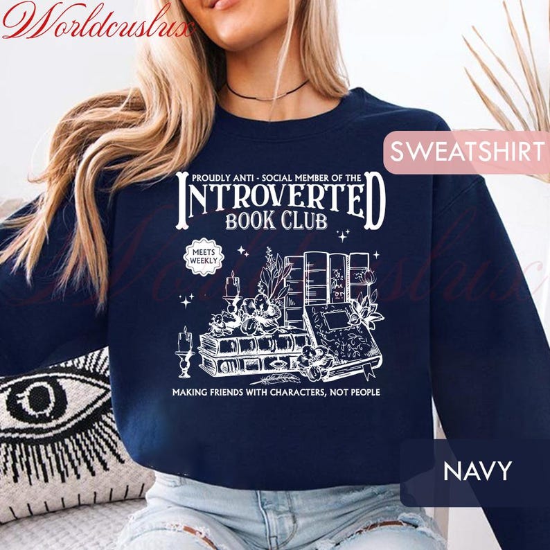 May include: Navy blue sweatshirt with white graphic text: "INTROVERTED BOOK CLUB" and "MAKING FRIENDS WITH CHARACTERS, NOT PEOPLE." The design includes illustrations of books, candles, and floral elements. The word "SWEATSHIRT" is in a pink box.