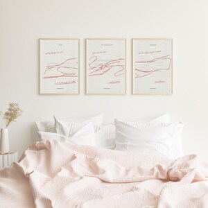 May include: Three framed art prints with red line drawings and text on a cream background. The prints are displayed above a bed with a pink duvet and white pillows. The art has a minimalist aesthetic.