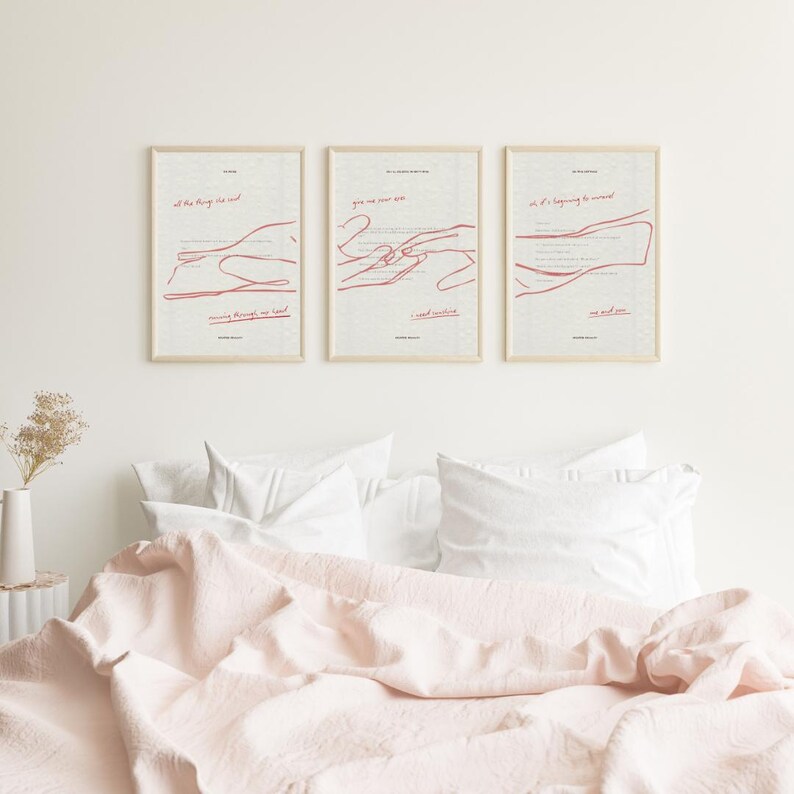 May include: Three framed art prints with red line drawings and text on a cream background. The prints are displayed above a bed with a pink duvet and white pillows. The art has a minimalist aesthetic.