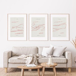 May include: Three framed art prints with minimalist designs. Each print features a light background with red line art and text. The prints are displayed above a beige sofa with wooden coffee tables.
