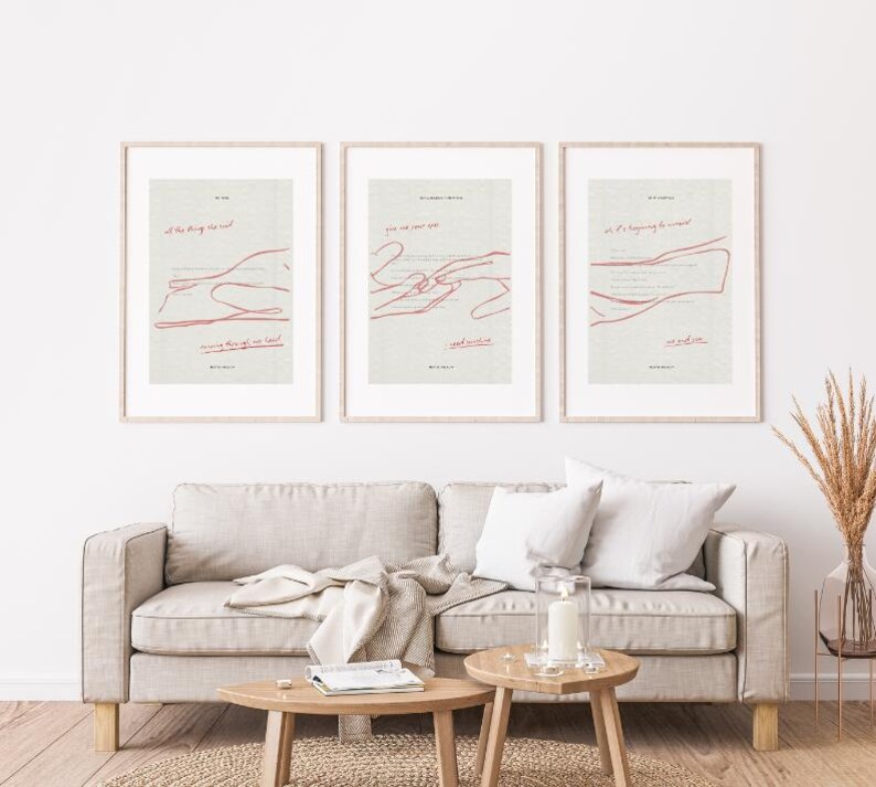 May include: Three framed art prints with minimalist designs. Each print features a light background with red line art and text. The prints are displayed above a beige sofa with wooden coffee tables.