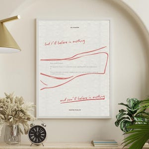 May include: A framed art print featuring the text "But I'll believe in anything" in red script. The print also includes a red line drawing and the text "and you'll believe in anything". The print is displayed on a wooden shelf with a clock and vase.