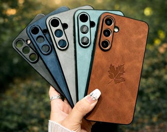 May include: A collection of five phone cases in various colors: black, navy blue, gray, teal, and brown. The brown case features a leaf design. Each case has a camera cutout.