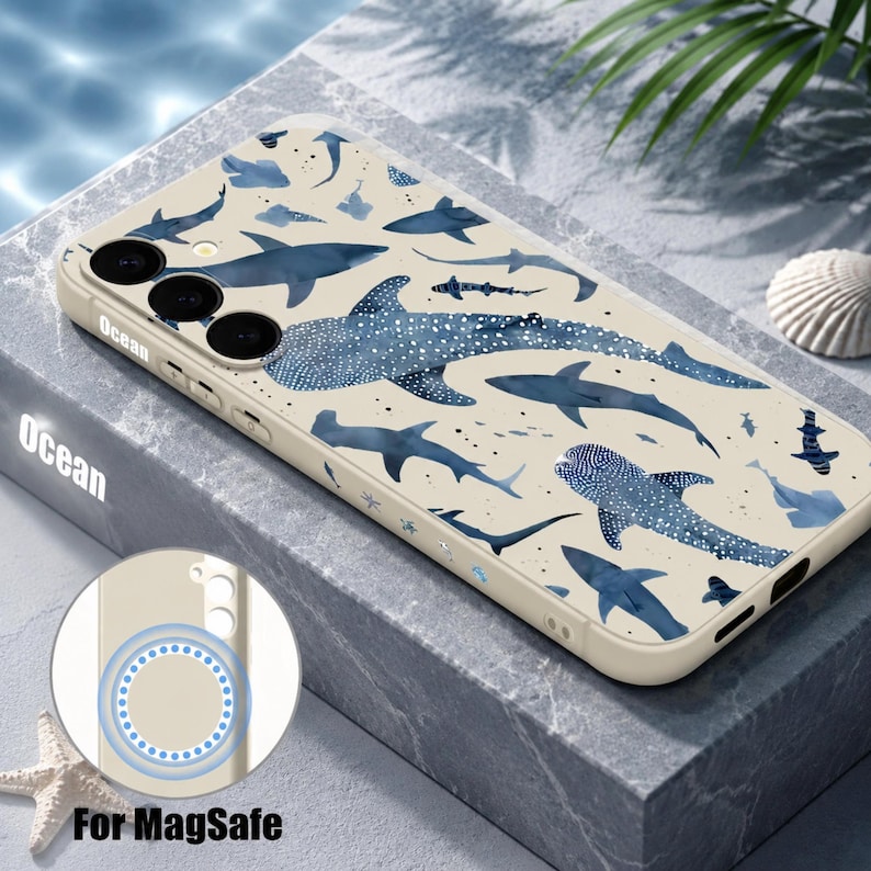 May include: A cream-colored phone case featuring a pattern of various blue sharks and whale sharks. The case includes a circular magnetic ring on the back for MagSafe compatibility and has cutouts for the camera lenses and side buttons.