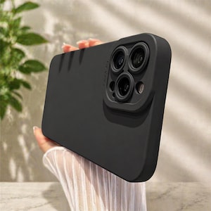 May include: A black phone case with a raised camera lens protector. The case has a smooth finish and is designed to fit a smartphone. The camera lens protector has three circular openings for the lenses.