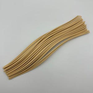 May include: A bundle of thin, light brown wooden reeds, arranged in a slightly curved shape. The reeds are smooth and appear to be of uniform length, suggesting they are for a craft or decorative purpose.