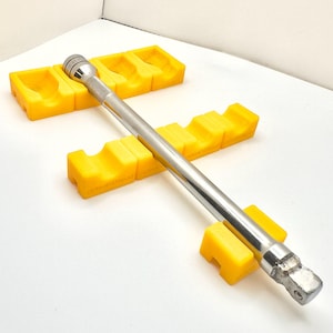 May include: A shiny, silver metal ratchet wrench is positioned diagonally across three bright yellow foam supports. The supports are arranged in a cross shape. The background is white.