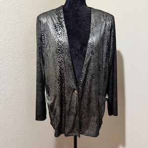 May include: A long-sleeved blazer featuring a metallic silver and black snakeskin pattern. The garment has an open front design with a single gold-toned button closure at the center and two side pockets. The fabric has a shimmering finish.