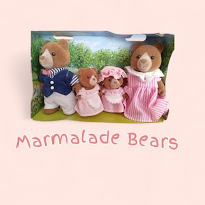 Puede incluir: Una familia de muñecos Osos Marmalade en un diorama. El oso padre lleva una chaqueta azul y pantalones blancos. La osa madre lleva un vestido a rayas rosas. Los niños llevan vestidos y delantales rosas. El texto "Marmalade Bears" está en la parte inferior.