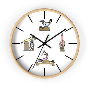 May include: A round wall clock with a light wood frame. The clock face is white with black hands and hour markers. The clock face features illustrations of people doing Pilates exercises in various positions.