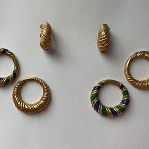 May include: Gold-toned jewelry set featuring two pairs of earrings and two rings. The earrings and one ring have a textured, twisted design. The other ring has blue and green enamel stripes. The jewelry is displayed on a white surface.
