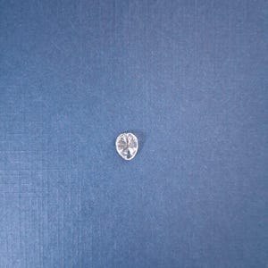 May include: A clear, oval-shaped gemstone with multiple facets, reflecting light. The gem is set against a textured, dark blue background, creating a contrast that highlights its brilliance. This gemstone could be used in jewelry.