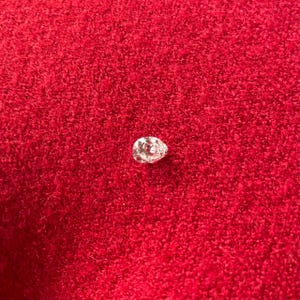 May include: A pear-shaped diamond, sparkling with facets, rests on a vibrant red textured surface. The gemstone's cut and clarity are highlighted against the contrasting background, showcasing its brilliance.