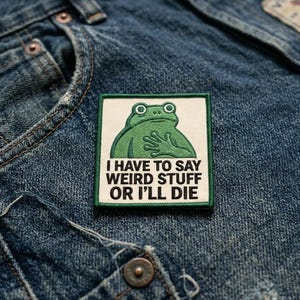 May include: A square patch with a green frog illustration and the text "I HAVE TO SAY WEIRD STUFF OR I'LL DIE" on a white background. The patch is bordered in green and is set against a blue denim background.