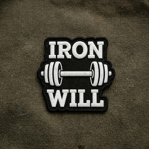 May include: Black and white embroidered patch with the words "IRON WILL" and a barbell design. The patch is rectangular with a black background and white stitching. The patch is on a textured, olive green fabric.