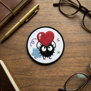 May include: Embroidered patch featuring a black creature holding a red heart. The patch has a white background with a black border, and includes a blue cloud, purple swirl, green cross, and red exclamation mark.