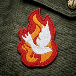May include: Embroidered patch featuring a white dove within a flame design. The patch has a red border with orange and yellow flames. The patch is on a green fabric background, with a button in the upper right corner.