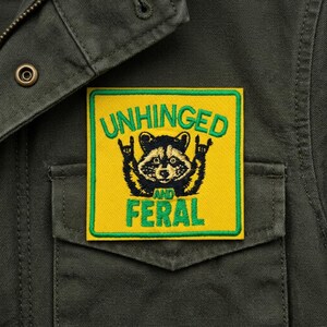 May include: A square patch with a yellow background and a green border. The patch features a raccoon with a rock-and-roll hand gesture and the words "UNHINGED AND FERAL" in green.