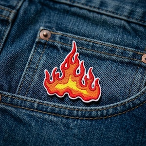 May include: Embroidered patch featuring a flame design in shades of yellow, orange, and red with a white border. The patch is affixed to the pocket of a blue denim garment, showcasing the patch's vibrant colors against the denim.