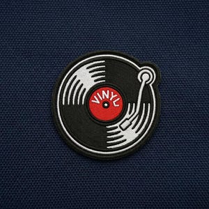 May include: Embroidered patch featuring a black vinyl record with white grooves and a red center. The word "VINYL" is printed in white on the red center. The patch has a white border and is set against a navy blue background.