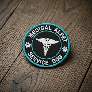 May include: Round patch with the words "MEDICAL ALERT SERVICE DOG" in white lettering on a black background, with a teal border. The center features a white caduceus symbol and paw prints.