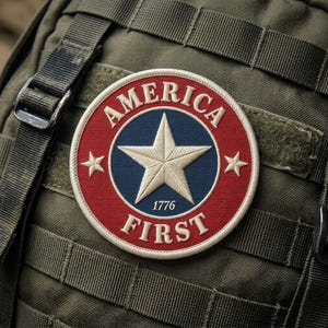 May include: A round patch with the words "AMERICA FIRST" in white lettering. The patch features a white star on a blue background, surrounded by a red border. The year "1776" is below the star. The patch is attached to a green backpack.