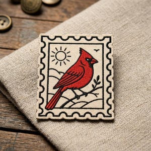 May include: Embroidered patch featuring a red cardinal bird perched on a branch, set against a landscape with a sun and a small bird. The patch is designed in a postage stamp style with a cream-colored background and black border.