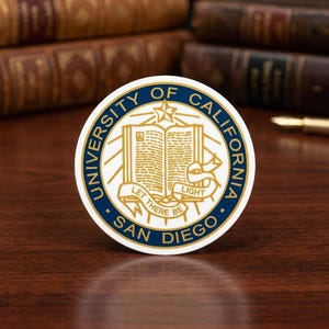May include: A round sticker featuring the University of California San Diego seal. The seal is white and gold with a blue border, and includes the text "University of California San Diego" and "Let There Be Light."