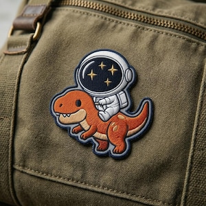 May include: Embroidered patch featuring an astronaut riding an orange dinosaur. The astronaut is wearing a white spacesuit and helmet with three gold stars. The dinosaur has a friendly expression and is outlined in blue.