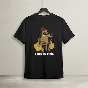 May include: Black t-shirt featuring an embroidered cartoon dog wearing a red hat, sitting in a chair surrounded by flames. The text "THIS IS FINE" is below the dog.