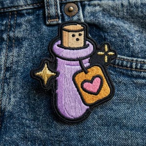 May include: Embroidered patch featuring a purple potion bottle with a cork stopper. A tag with a pink heart hangs from the bottle. Gold star and cross accents are on a black background. The patch is on a denim background.