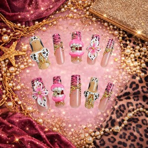 May include: A set of ten press-on nails featuring a variety of designs including pink tiger stripes, 3D pink lips with white teeth, white and black leopard print patterns, pink floral accents, and gold-toned chain embellishments with small crystals.
