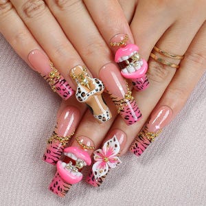 May include: Long acrylic nails featuring a nude base with pink and black animal print tips, accented with gold beads. Embellishments include 3D pink lips with gold teeth, a white and black leopard print bikini top, and a white and pink flower charm.