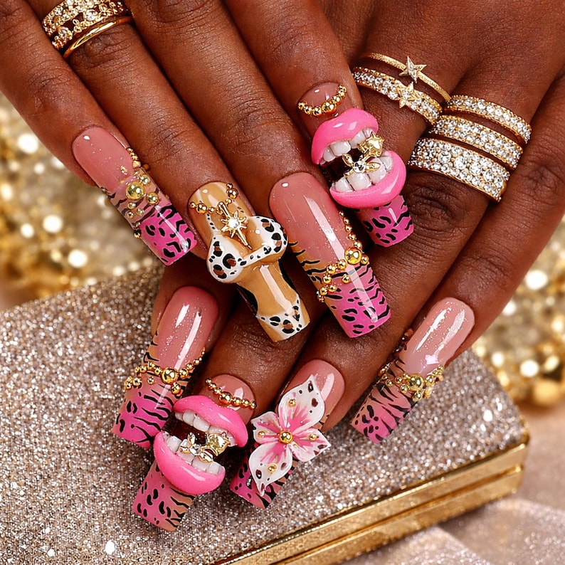 May include: Long square-shaped artificial nails featuring a nude base with pink and black animal print tips. Embellishments include 3D pink lips with white teeth, a leopard print bikini charm, a white and pink flower, and gold metallic beads.